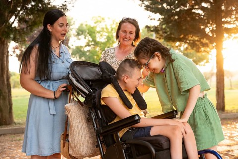 A family shares a joyful moment outdoors with two children. A girl with a tracheostomy and a boy