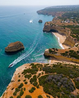Coastline with clear turquoise water, cliffs and a boat near the coast, aerial view, Albandeira,