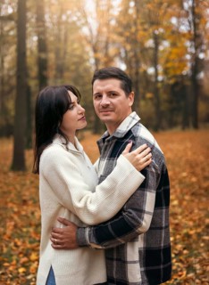 A couple embraces amidst a vibrant autumn woodland backdrop, capturing the essence of fall with