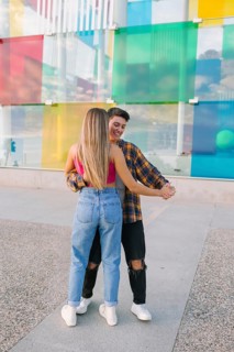 A joyful lesbian couple dances together in an urban setting, smiling and holding hands. The vibrant