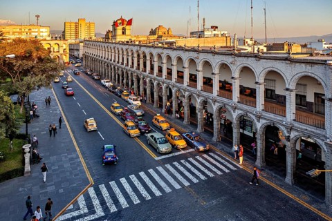 Urban scene at sunset, historic arcades, busy street with traffic and flags, The arcades at Plaza