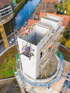 Building construction project near a river, construction workers and crane visible, extension of