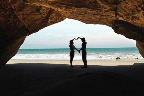 Silhouettes of a young couple forming a heart with their hands in a stunning beach cave in Mancora,