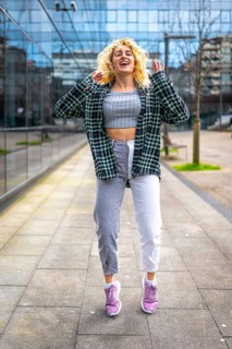 Carefree young woman jumping and dancing in urban city street, enjoying freedom and expressing