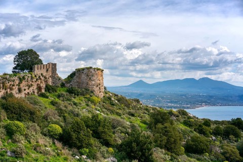 Stunning view of ancient stone fortress ruins on a lush hilltop, overlooking the sparkling ocean in
