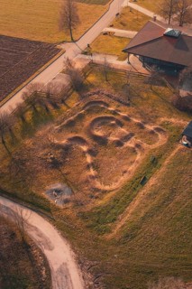 Aerial view of a mound with winding paths surrounded by country road and autumn landscape, bike
