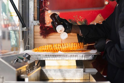 A perfectly fried spiral tornado potato on a skewer, drizzled with flavorful sauce, being prepared