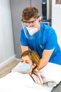 Cranial osteopathy by a physiotherapist with protective measures for a patient on the stretcher.