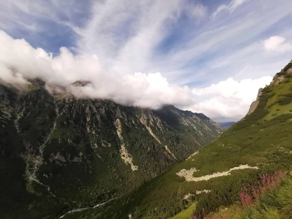Extensive valley with lush slopes under blue skies with thick clouds above the mountain peaks,