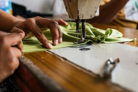 A close up shot of a sewing machine with asian seamstress hands skillfully guiding green fabric