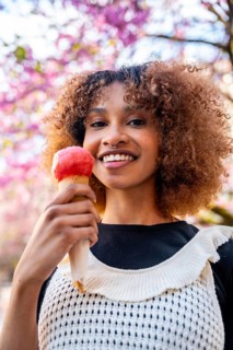 Smiling young woman enjoying an ice cream cone while standing under a blooming tree, surrounded by