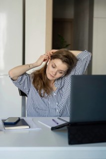 Woman in a striped shirt at home, adjusting her earphones while working on a laptop. A phone,