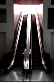 A starkly lit escalator captured between moments of use, creating a sense of movement amidst a