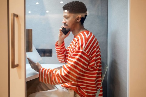 A professional seated in a private coworking booth making a phone call while holding a document.