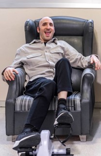 A man enjoys relaxation and exercise on a chair with a pedal machine in a mental health residence.