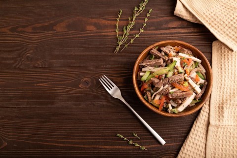 Meat salad with beef and vegetables in wooden bowl on brown wooden background and linen textile.