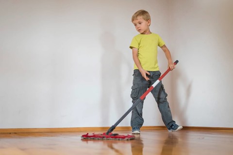 A 6-year-old boy cleaning the wooden floor with a mop