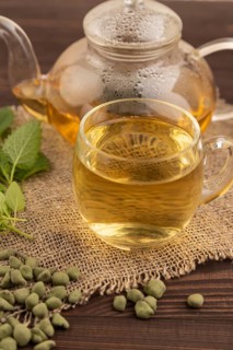 Green oolong tea with herbs in glass on brown wooden background and linen textile. Healthy drink