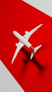 A sleek commercial airplane soars through the sky, casting a distinct shadow on a vibrant red