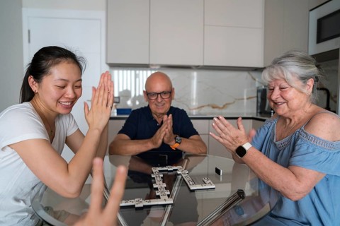 A joyful multigenerational family playing dominoes around a kitchen table. Three family members are