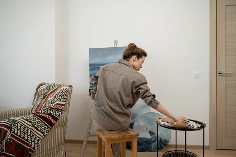 An artist works intently on a sea inspired painting in a cozy home studio. The scene is peaceful,