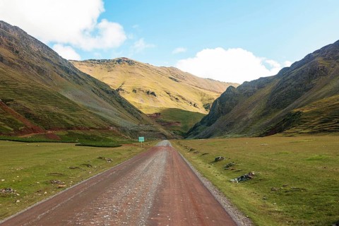 A captivating view of a dirt road winding through the vibrant, green and golden mountain valleys of