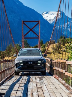 SUV driving over old-style orange suspension bridge, river Rio Nadis south of Cochrane, mountain