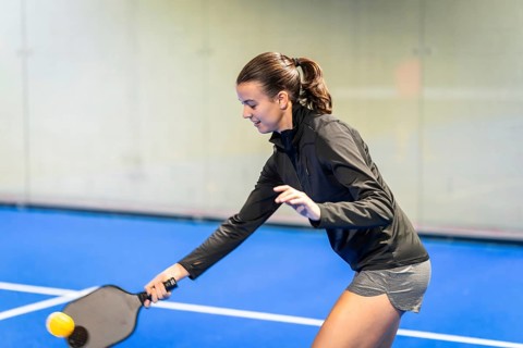 Young woman actively playing pickleball, holding a paddle and preparing to hit the ball on a blue
