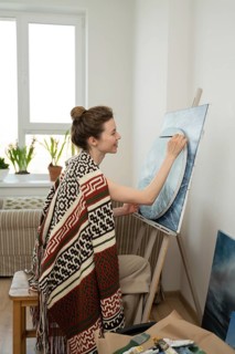 A woman artist paints on a canvas in a cozy room with natural light streaming through a window,