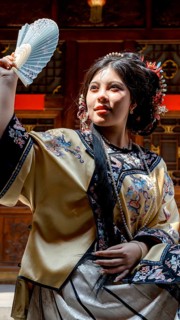 A young woman in Qing Dynasty attire poses elegantly in Pingyao, China, holding a delicate fan. Her