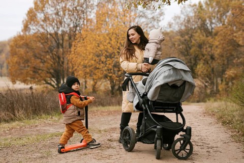 A family enjoys a leisurely autumn walk in a scenic forest. The mother, carrying a baby, talks to