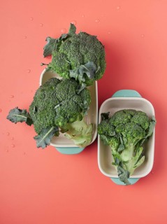 Whole fresh broccoli pieces on baking pans on a pink table