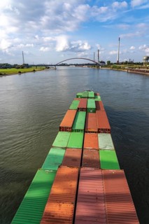 The Dutch cargo ship Vrido, loaded with containers, on the Rhine near Duisburg, descending, behind