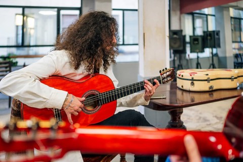 Latin man with long hair playing red bass guitar in studio