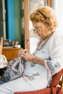 Senior woman wearing glasses concentrating on sewing a piece of patterned fabric while sitting