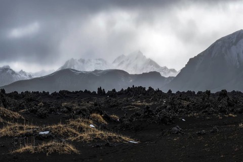 Moody skies loom over the rugged, volcanic terrain of Iceland's Highlands. Snow-dusted peaks rise