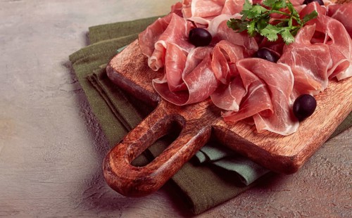 Sliced prosciutto, on a cutting board, with olives and herbs, snack, breakfast, no people