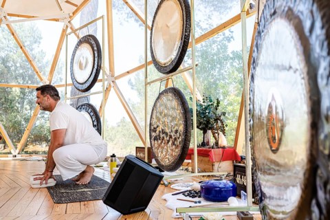 A male sound therapist in a serene geodesic dome setting prepares for a sound therapy session with