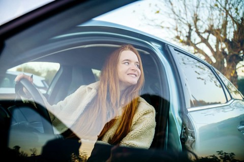 A beautiful pregnant woman with red hair sits comfortably in a car, looking outside with a peaceful
