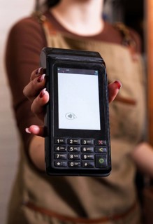 A woman offers a contactless payment terminal in a cozy cafe setting, highlighting modern