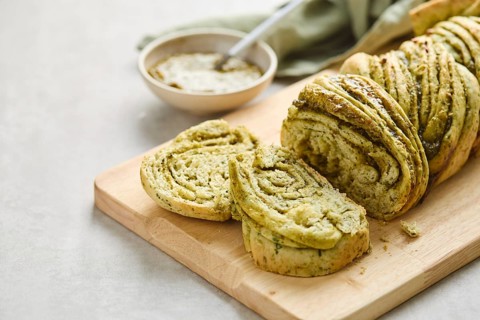 Baked homemade savoury babka plaited bread loaf flavoured with pesto on wooden bread board. Close