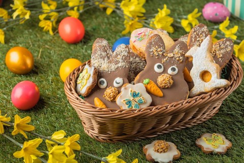 Decorated Easter cookies in a basket surrounded by colorful eggs on grass
