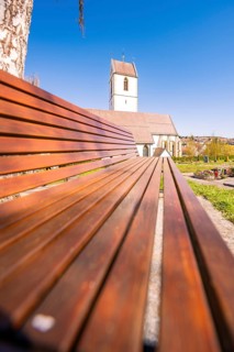 Wooden bench in dramatic perspective with a church in the background under a blue sky, Aidlingen,