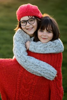 Two siblings, a young girl and her little brother, are warmly dressed in colorful knitwear, sharing