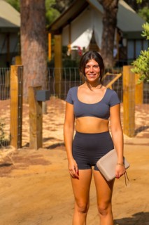 Young woman smiling and holding her purse while standing on a dirt path at a glamping resort,