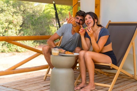 Happy couple eating breakfast and pointing at something while sitting on the wooden patio of their
