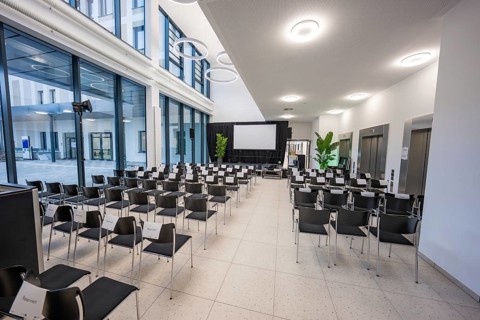 Modern conference room with rows of chairs and plants, a stage in front, Calw Hospital, Germany