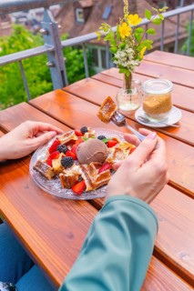 Person enjoying waffles with berries and ice cream on a balcony with a view, Cafehäusle Calw, Black