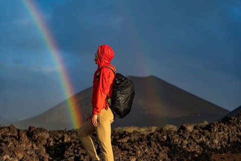 An adventurer in a red jacket and backpack explores the volcanic terrain of Timanfaya National