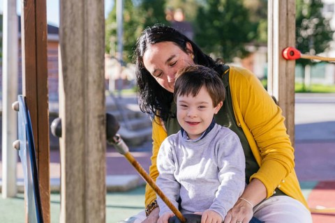 A joyful moment of a mother and her child with Down syndrome on playground equipment, enjoying a